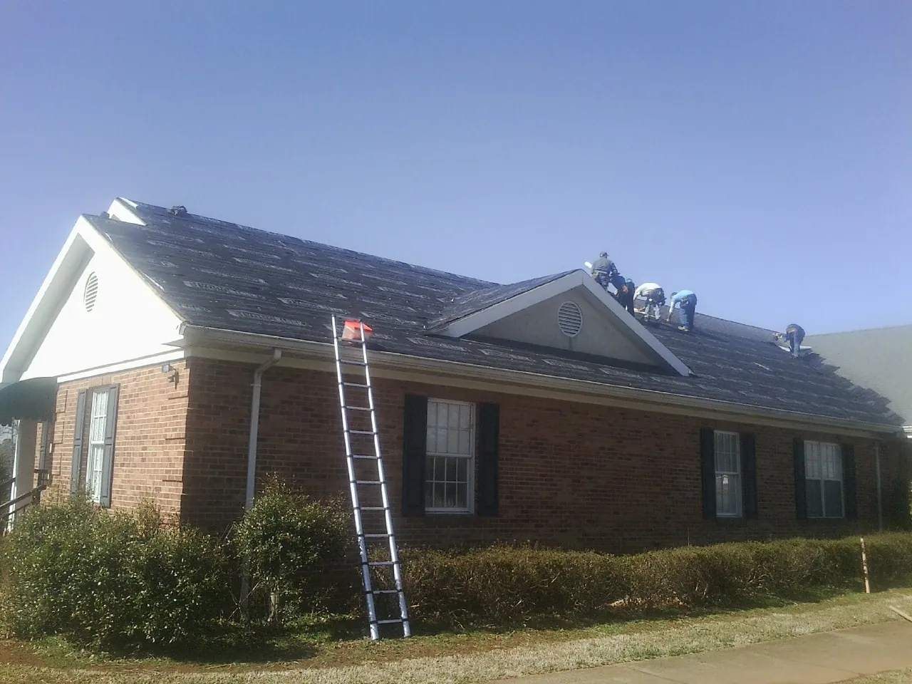 Crew tearing shingles off a brick ranch roof with a ladder set — Metal Roof Repair work by our crew in Little River
