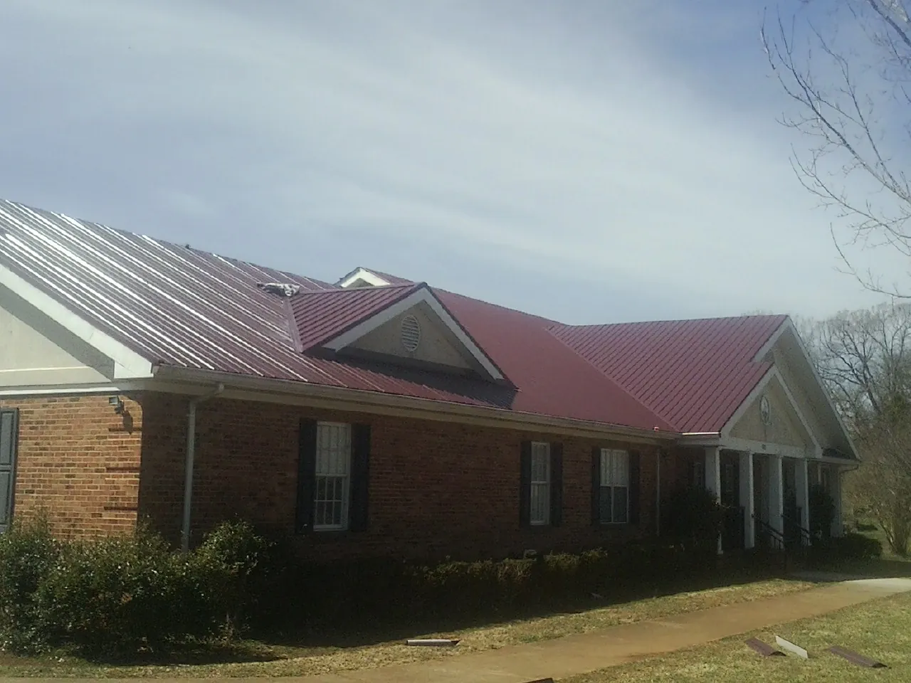 Red metal roof with gabled entries on a long brick building, from a Hail Damage Roof Repair job in Little River