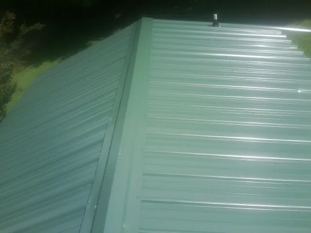 New green metal panels meeting at the ridge of a roof — Flat Roof Repair work by our crew in Little River