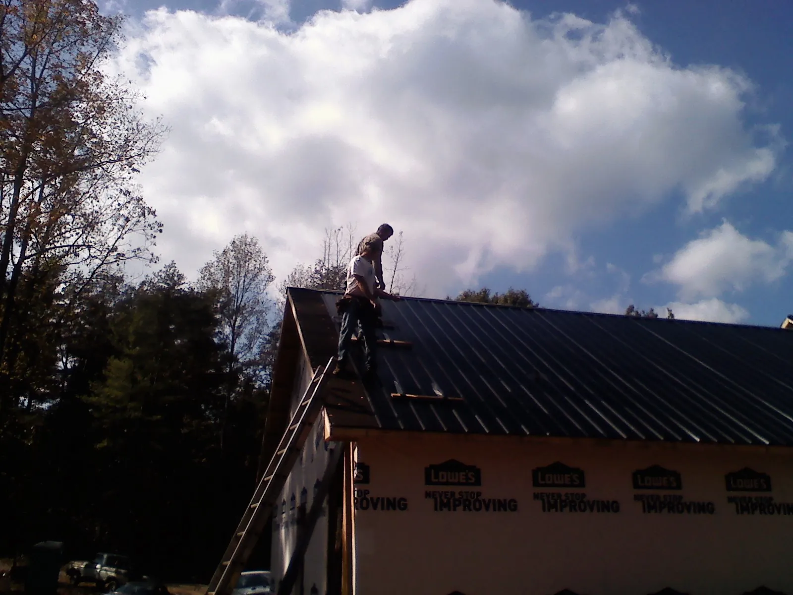 Roofer fastening dark metal panels high against a cloudy sky, from a Roof Inspection job in Little River