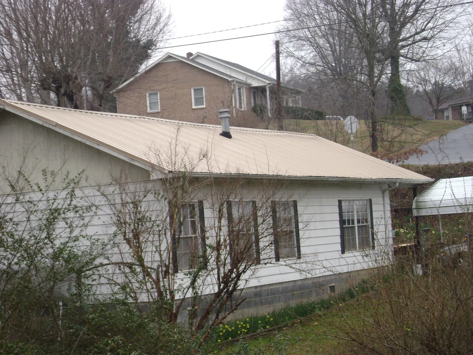 Tan metal roof on a white sided house set into a hillside — Commercial Roofing by Roofing Brothers in Little River