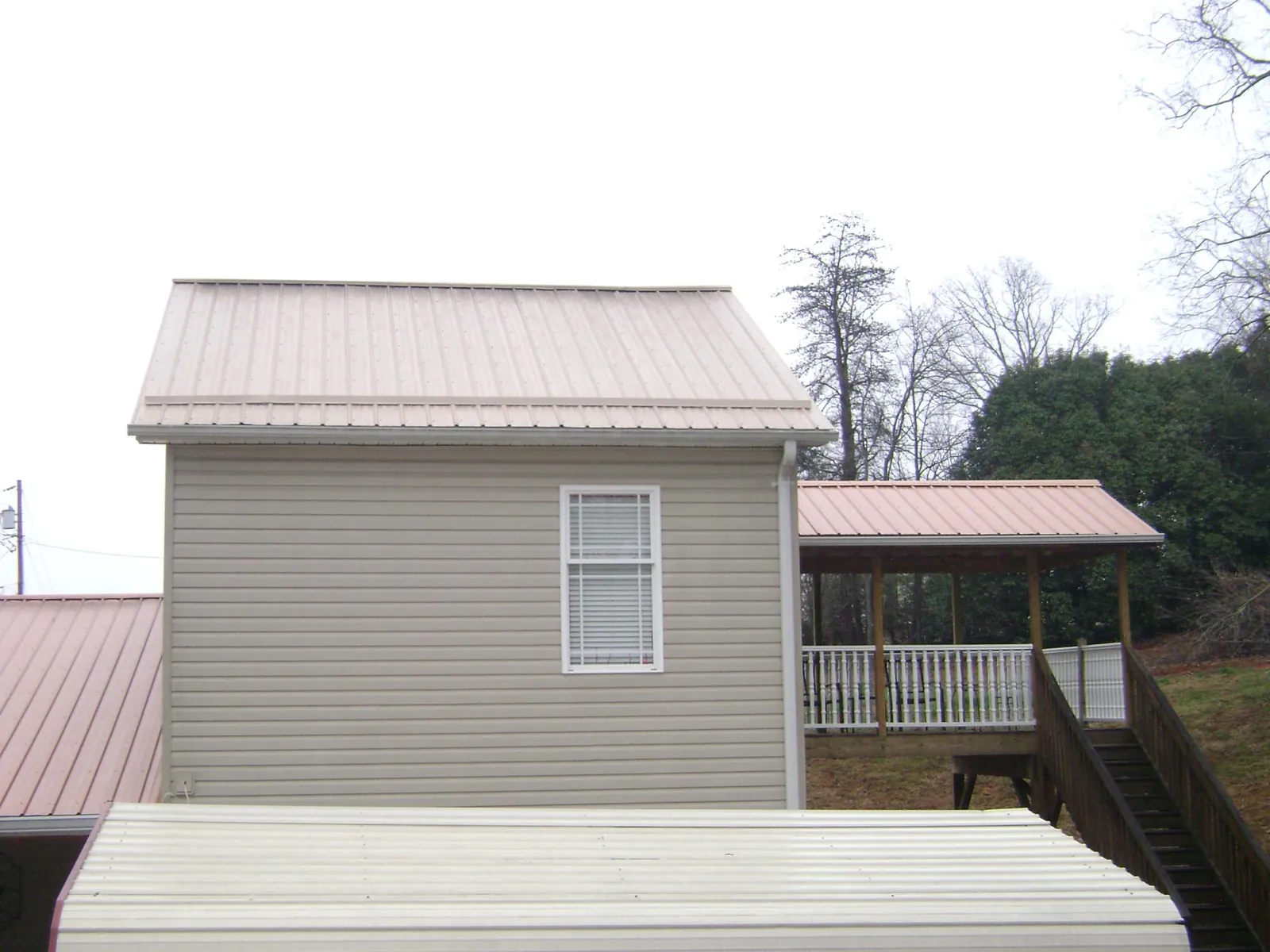 Tan metal roofs on a two story addition and attached porch, from a Roof Replacement job in Little River
